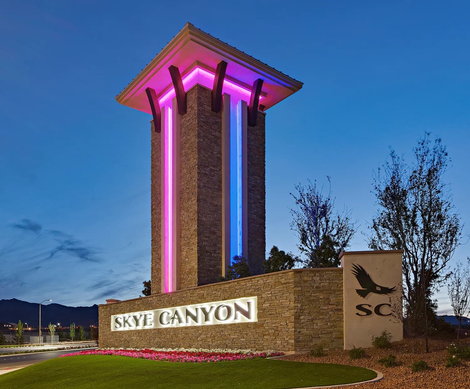 The Skye Canyon community entrance monument sign, lit at dusk, with the Spring Mountains in the background.