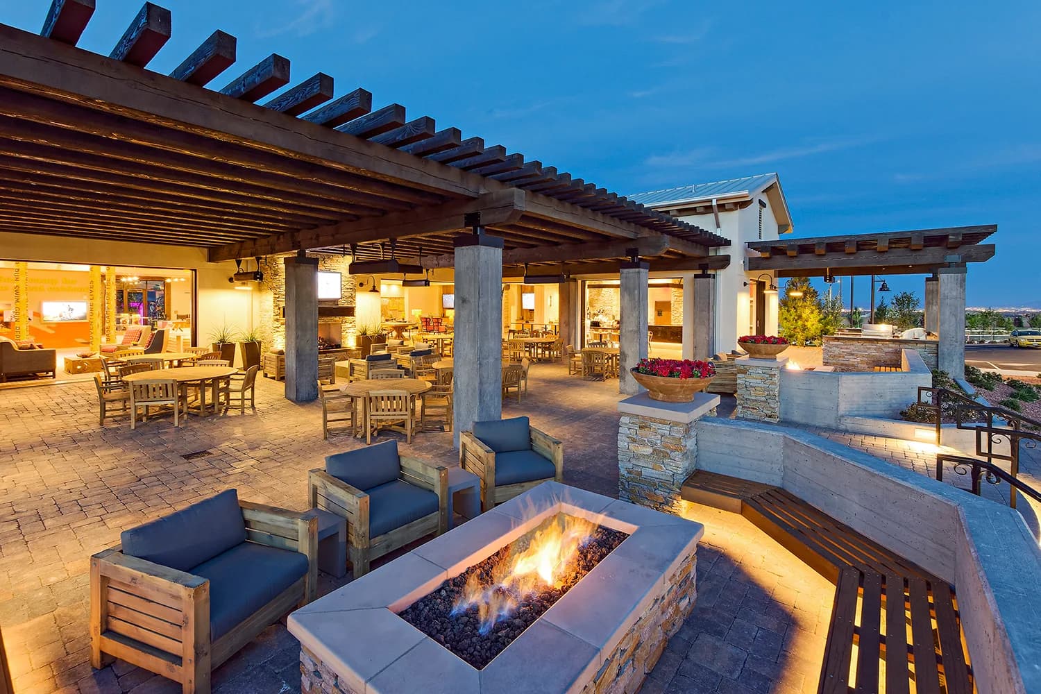 An outdoor lounge patio at the Skye Canyon community center, with a fire pit, pergola and seating area at dusk.