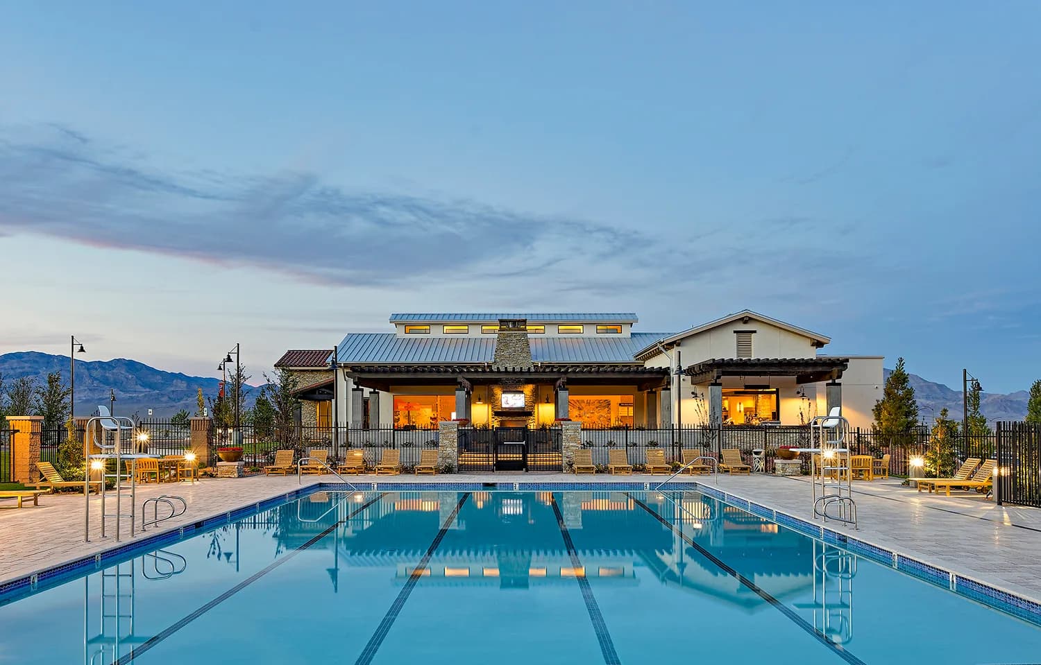 The Skye Canyon community center's lap pool at dusk, with the clubhouse building behind it.